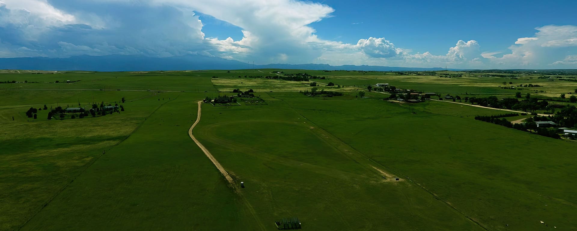 Aerial view of a lure coursing field: green pasture under a big Colorado sky, with the course track cut into the grass.